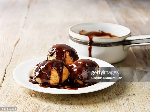 profiteroles with hot chocolate sauce on white plate, rustic wooden table - profiterole stock-fotos und bilder