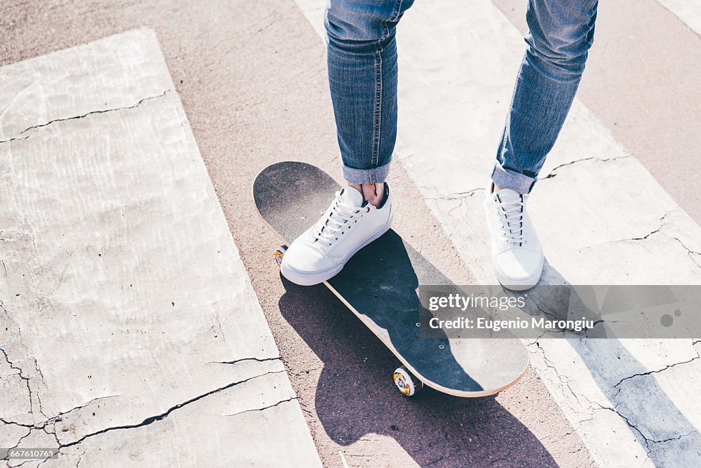 Legs and feet of young male skateboarder on pedestrian crossing