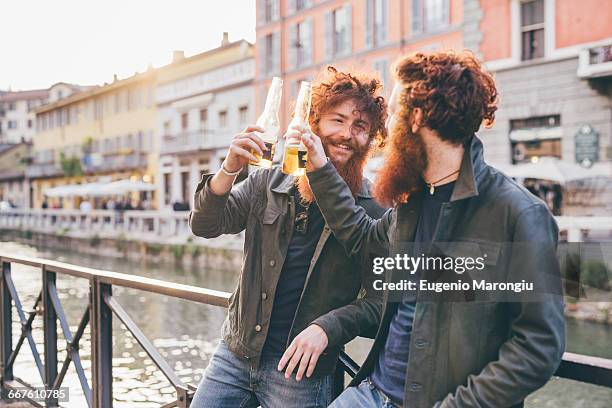 young male hipster twins with red hair and beards making a toast on canal waterfront - gémeo idêntico imagens e fotografias de stock