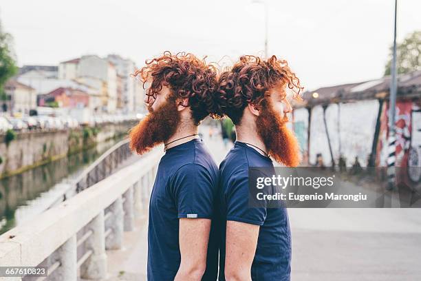 portrait of young male hipster twins with red hair and beards back to back on bridge - twin fotografías e imágenes de stock