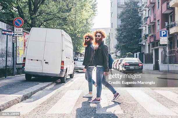 young male hipster twins with red hair and beards strolling on pedestrian crossing - identical twin stock pictures, royalty-free photos & images