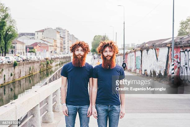 portrait of young male hipster twins with red hair and beards standing on bridge - zwilling stock-fotos und bilder
