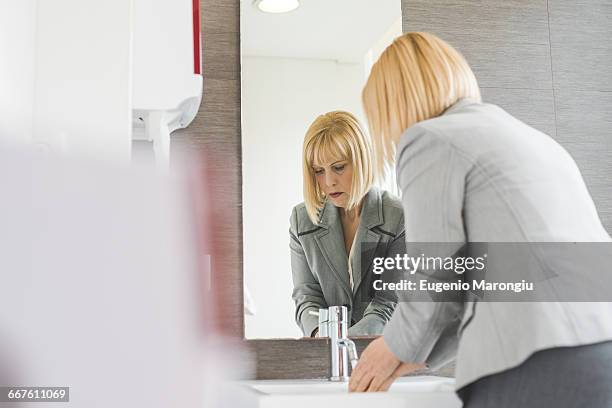 mature businesswoman washing hands in office powder room - パウダールーム　女性 ストックフォトと画像