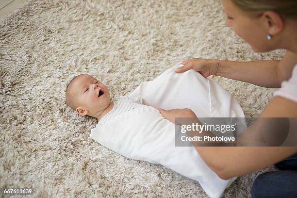 swaddling step 5. mother wrapping and tucking in baby boy with blanket - babydeken stockfoto's en -beelden