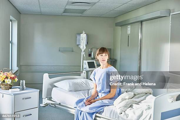 patient sitting on hospital bed wearing hospital gown - hospital gown imagens e fotografias de stock