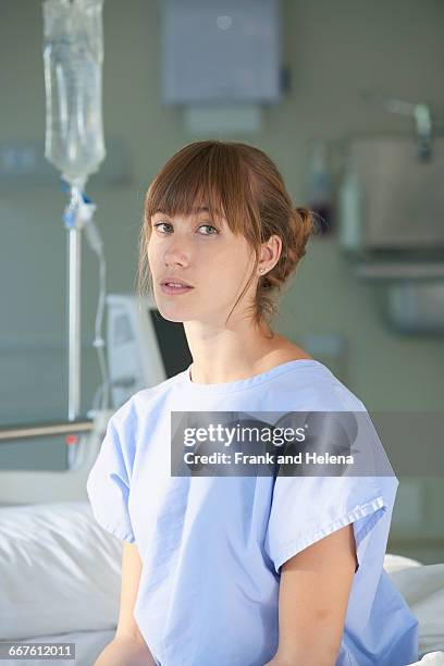 woman sitting on hospital bed wearing hospital gown - junge frau bett sitzen blick in die kamera stock-fotos und bilder