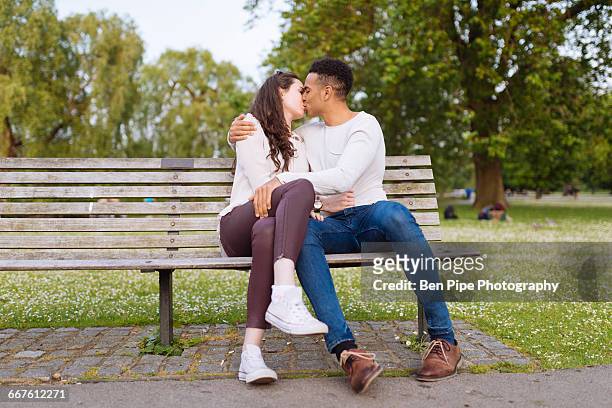 young couple on park bench kissing - couple kissing stock-fotos und bilder