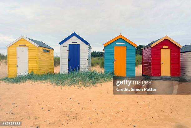 front view of a row four multi-coloured beach huts, southwold, suffolk, united kingdom - southwold stock pictures, royalty-free photos & images