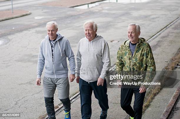 senior friends wearing sports clothes walking side by side - 3 old men jogging stock-fotos und bilder