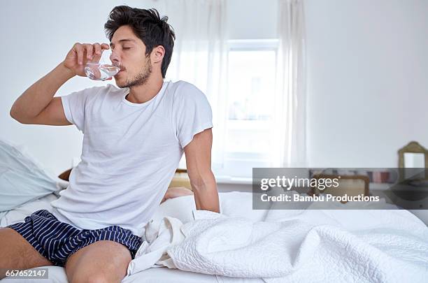 man sitting in bed drinking water - hang over stock pictures, royalty-free photos & images