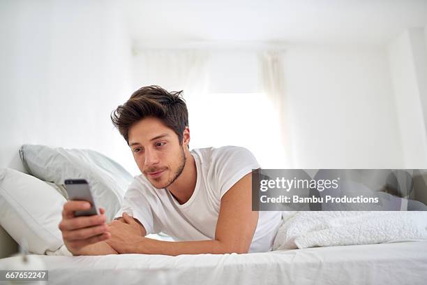 man with cell phone in bed - man lying on sofa stock pictures, royalty-free photos & images