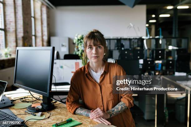 portrait of young woman standing in startup business space - rolling up sleeve stock-fotos und bilder