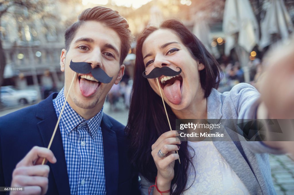 Friends making fake mustaches selfie on sunset