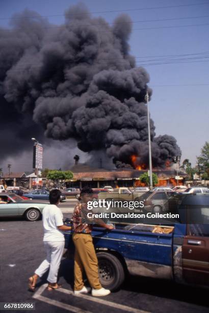 People look across the street from Viva Shopping center amongst a billowing fire during widespread riots that erupted after the acquittal of 4 LAPD...