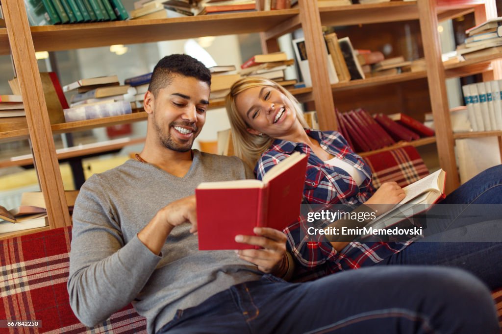 Multiétnico jovem estudante casal desfrutar de leitura de livros na biblioteca.