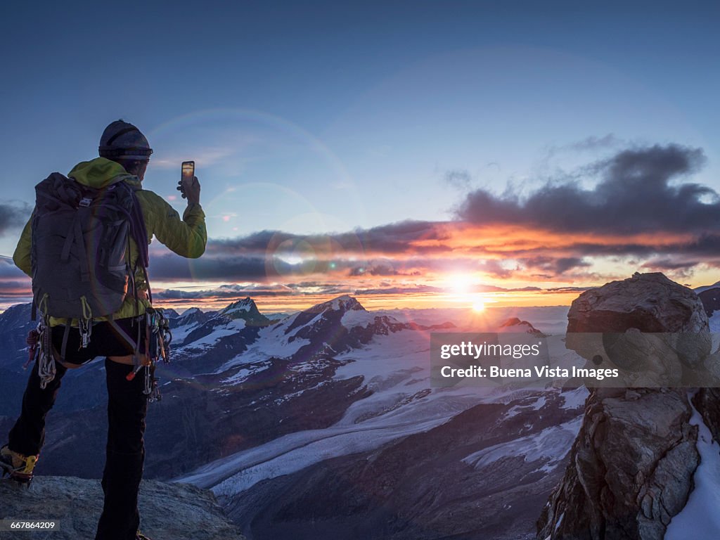 Climber on a peak photographing sunrise with smart