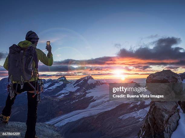 climber on a peak photographing sunrise with smart - take pictures stock-fotos und bilder