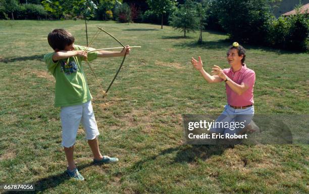 Daniel Prevost kneels with an apple on his head while his son Erling takes aim with a bow.