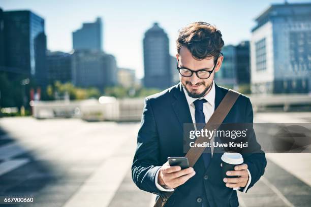 young businessman having coffee while using smart phone - mann anzug gebäude objekt draussen stock-fotos und bilder