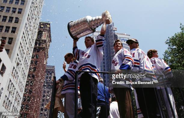 Brian Leetch of the New York Rangers holds the Stanley Cup Trophy as his teammates Mark Messier and goalie Mike Richter ride along with him during...