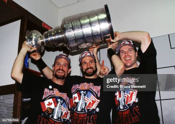 Ken Daneyko, Bruce Driver and John MacLean of the New Jersey Devils hoist the Stanley Cup Trophy over their heads in the locker room after the Devils...