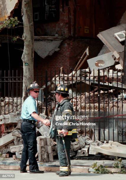 Firefighters shake hands after completing their work at an apartment building that partially collapsed July 13, 2000 at Second Avenue and East...