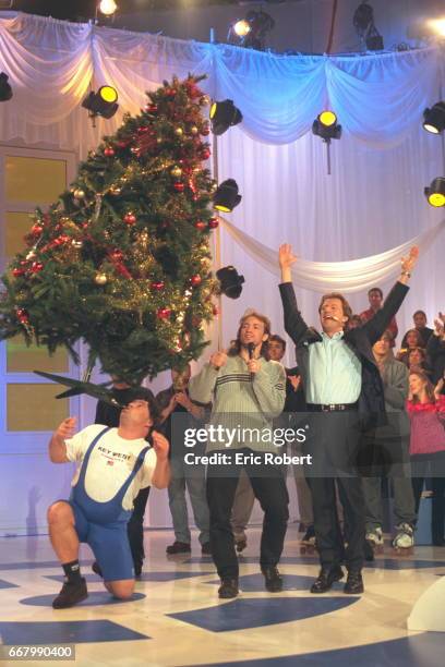 Un homme tenant un énorme sapin de noël avec sa bouche devant l'animateur Vincent Perrot avec le patineur artistique Philippe Candeloro.