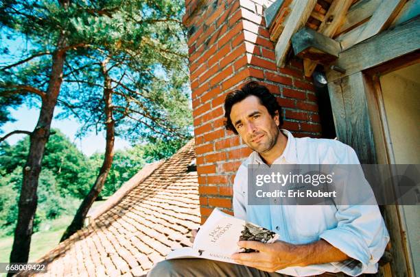 Nicolas Vanier sits on the roof of his house with a book from Jack London that he has read as a child.