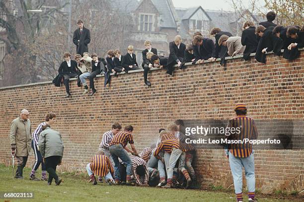 View of various pupils of Eton College, watched by fellow pupils sitting on the wall, playing the Eton Wall game between a team of Collegers and a...