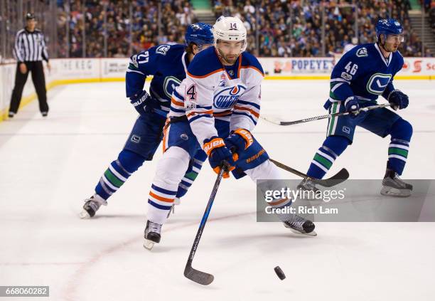 Jordan Eberle of the Edmonton Oilers corrals the loose puck after getting past Ben Hutton and Jayson Megna of the Vancouver Canucks in NHL action on...