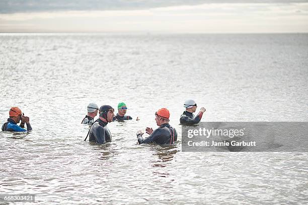 a group of sea swimmers stood in the sea talking - swimming stock pictures, royalty-free photos & images