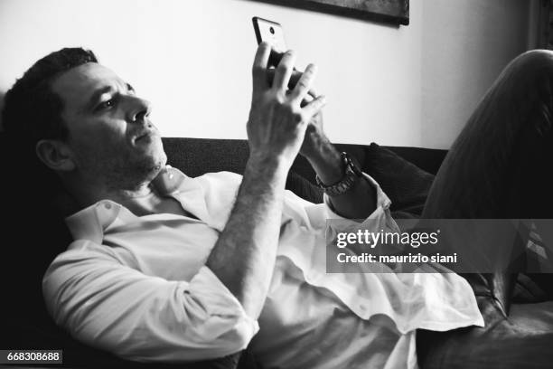 man relaxing on couch using cell phone - abbigliamento casual stock pictures, royalty-free photos & images