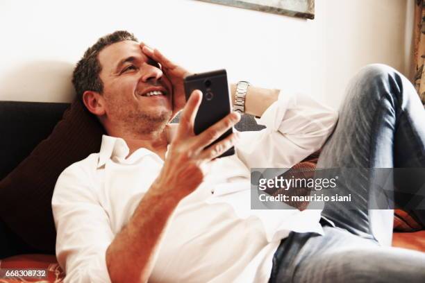 man relaxing on sofa using  smartphone - capelli grigi stock pictures, royalty-free photos & images