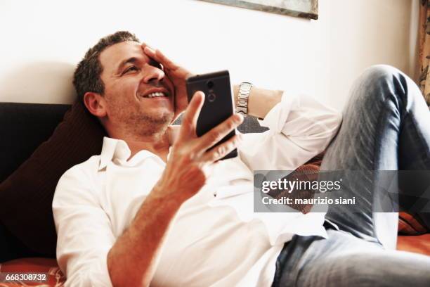 man relaxing on sofa using  smartphone - serenità imagens e fotografias de stock