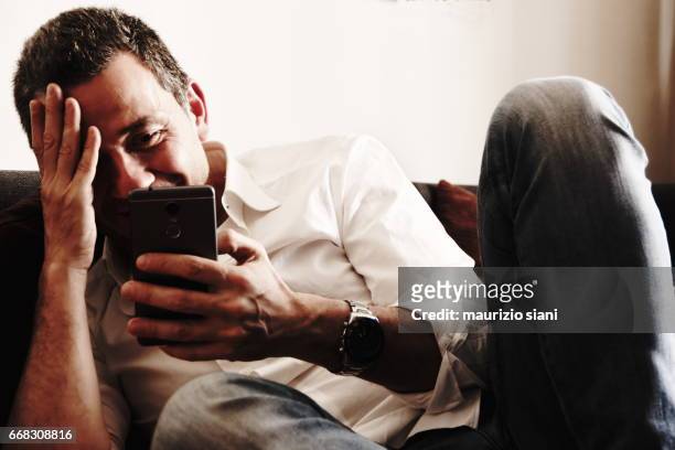 man relaxing on couch using cell phone - capelli grigi stock pictures, royalty-free photos & images