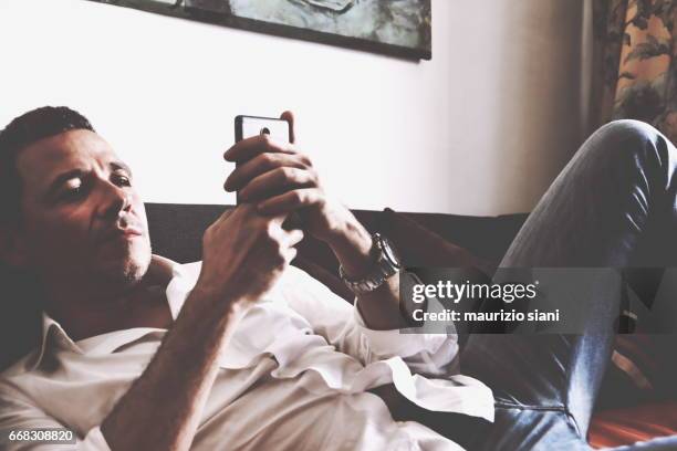 man relaxing on sofa using  smartphone - sorridere stockfoto's en -beelden