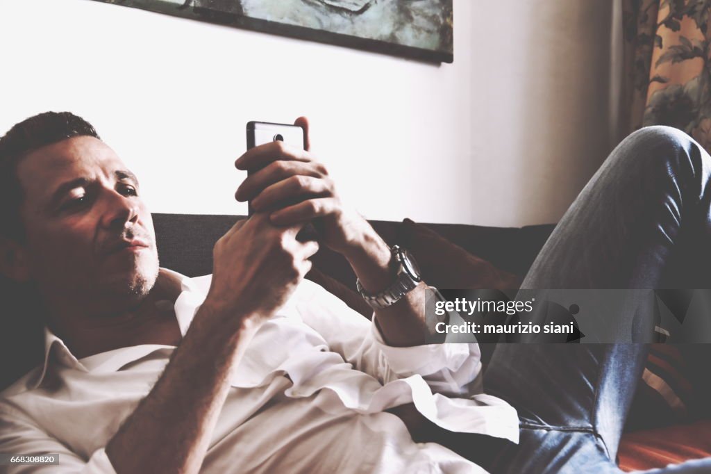 Man relaxing on sofa using  smartphone