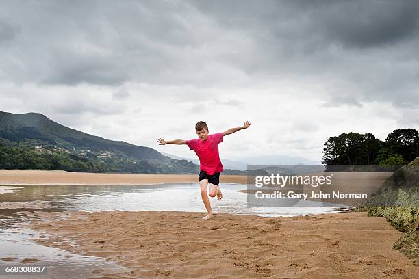 boy with arms outstretched running on beach - run shirt stock-fotos und bilder