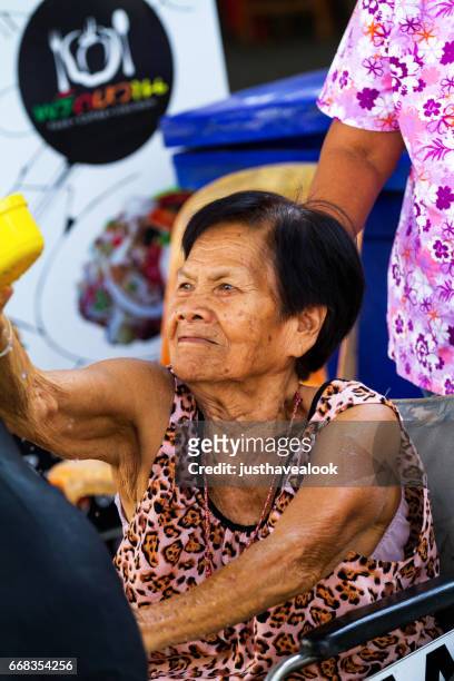 mujer senior thai en silla de ruedas jugar songkran - sorglos fotografías e imágenes de stock