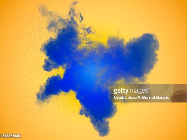 explosion of a cloud of powder of particles of  color blue on a orange background - color vibrante stock-fotos und bilder