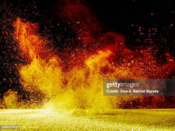 explosion of a cloud of powder of particles of orange and yellow color on a black background - caer stockfoto's en -beelden