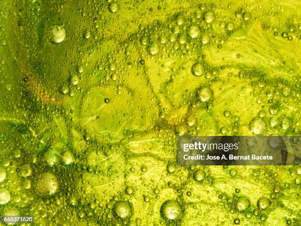 full frame of the textures formed by the bubbles and drops of oil in the shape of circle floating on a gold and green colors background - satén foto e immagini stock