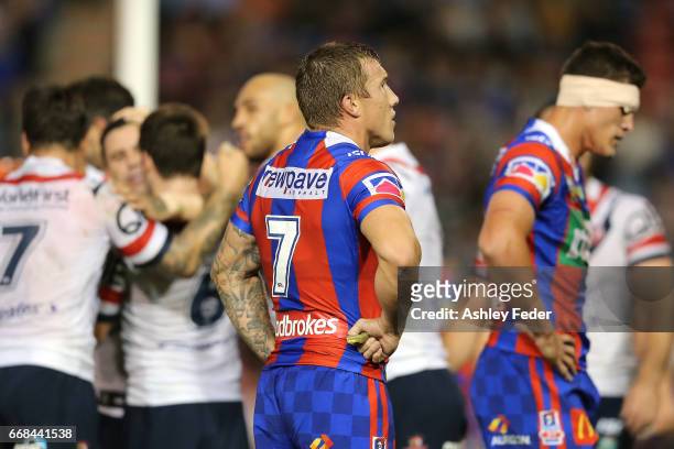 Trent Hodkinson of the Knights looks dejected with Roosters celebrating in the background during the round seven NRL match between the Newcastle...