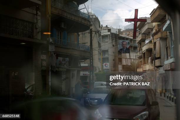 Crucifix hanging between buildings is refelcted on a shop window during a procession marking Holy Friday in a Christian-dominated neighbourhood of...