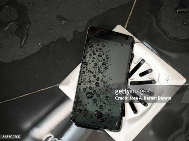 smart mobile phone dropped on the floor of a shower next to the drain with water - tecnología foto e immagini stock