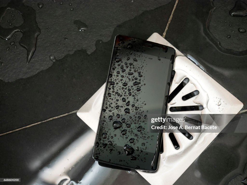 Smart mobile phone dropped on the floor of a shower next to the drain with water