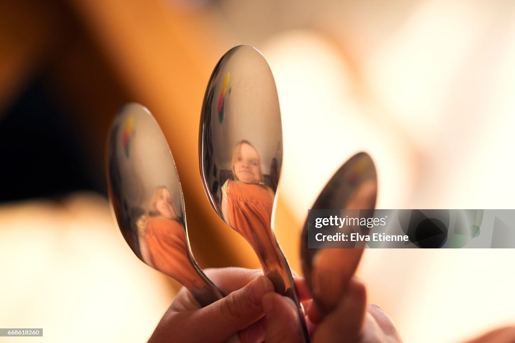 Child pulling silly face, reflected in spoons