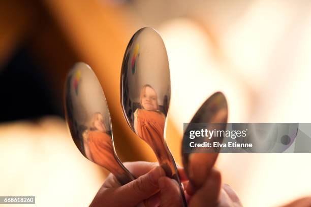 child pulling silly face, reflected in spoons - distorted reflection stock pictures, royalty-free photos & images