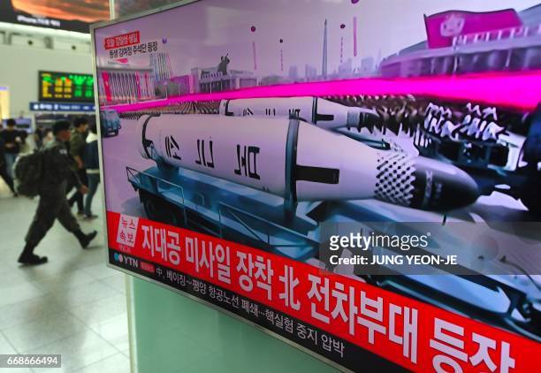 People walk past a television screen broadcasting live footage of a parade to mark the 105th anniversary of the birth of North Korea's founder Kim...