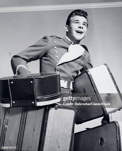 1950s SMILING BELLBOY CARRYING FOUR BAGS OF LUGGAGE